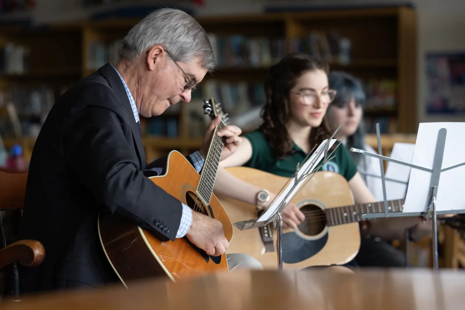 Joe Hetko playing acoustic guitar beside a young guitarist reading from a music stand.