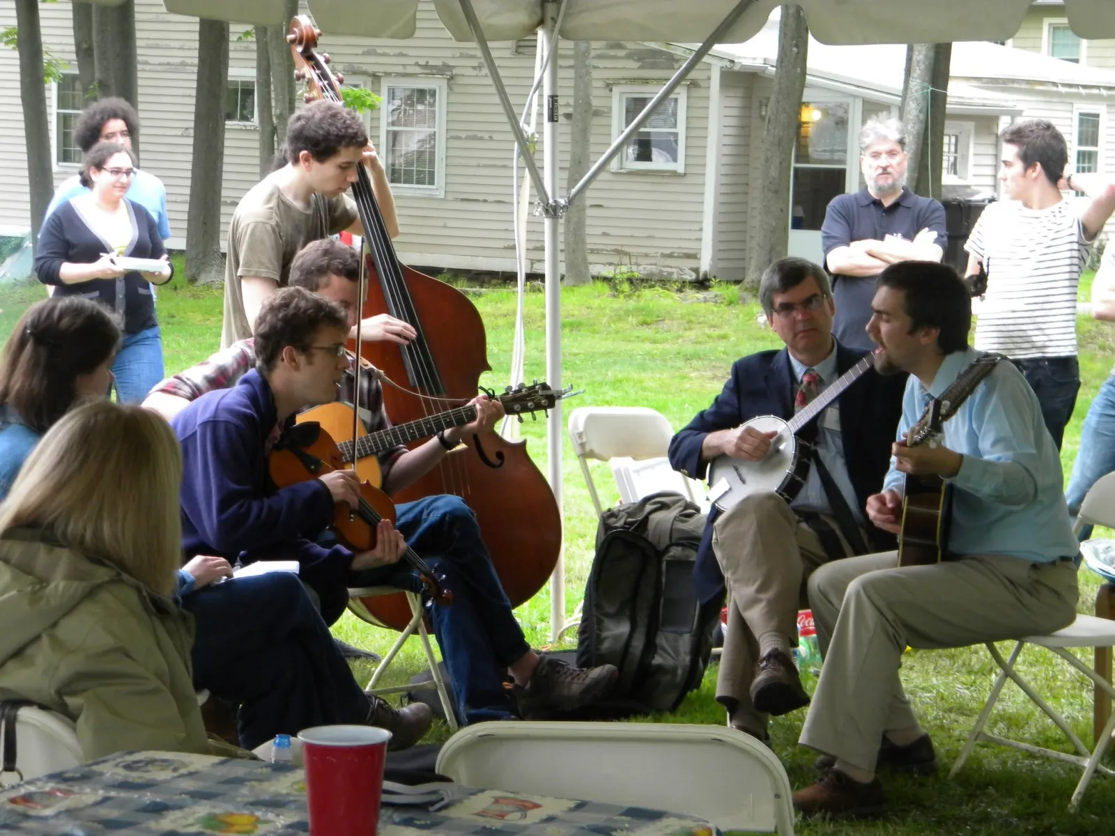 Joe Hetko playing banjo in an outdoor jam under a tent, surrounded by musicians on fiddle, guitar and upright bass.